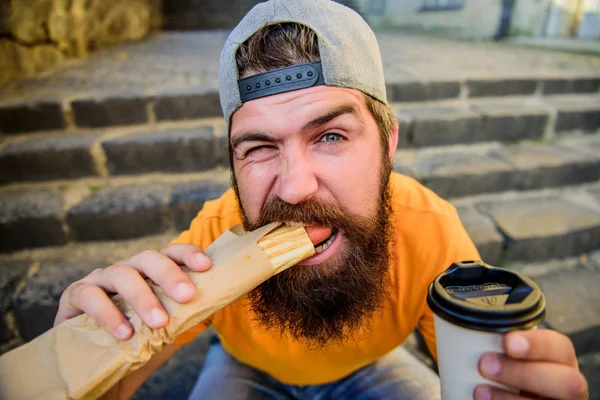 A comer depressa. Homem barbudo a comer sanduíche de cachorro quente. O caucasiano gosta de comer fora. Hipster comer cachorro quente e descansando em escadas ao ar livre — Fotografia de Stock