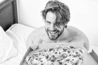 Adam pizza kutusu sit yatak yatak odası ya da otel odasında tutar. Evde yatakta lezzetli bir pizza yemek parlak bir apartman dairesinde öğrencidir. Gömleksiz seksi adam yatakta pizza ile görüntü kırpılmış. Yatakta yemek.