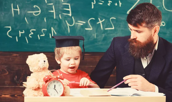 Wiskunde les concept. Vader leert zoon wiskunde. Leraar in formele slijtage en leerling in mortarboard in de klas, schoolbord op achtergrond. Enthousiaste jongen studeren met leraar — Stockfoto