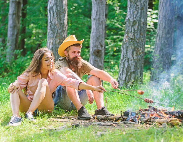 Couple friends prepare roasted sausages snack nature background. Hike picnic traditional roasted food. Hipster and girl roasting food. Camping activity. Couple in love camping forest roasting sausage
