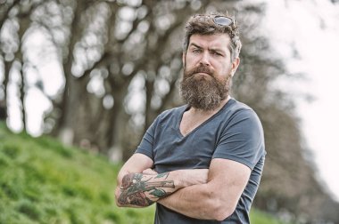 Hipster emin tutun çarpı işareti kollar göğüs üzerinde sakallı. Sakallı hippi acımasız maço. Kuaför kavramı. Bıyık ciddi bir yüz emin doğa arka plan ile sakallı adam. Gözlüklü sakallı adam