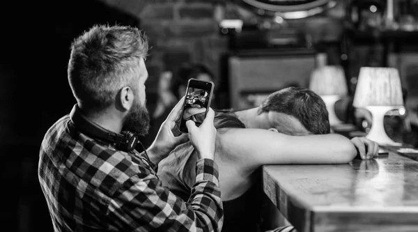 Man drunk fall asleep and guy with smartphone. Hipster taking photo drunk friend. Drunk friends in bar. Fall asleep at bar counter. Take photo to remember party. Hipster making fun of drunk friend