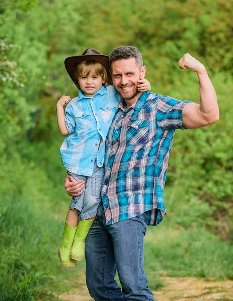 strong father and son in cowboy hat on ranch. kid in rubber boots. happy man dad in forest. human and nature. family day. happy earth day. Eco farm. small boy help father in farming. strong bonds