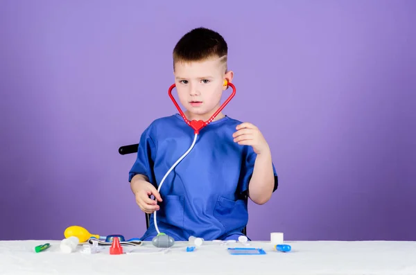 El niño pequeño médico se sienta en la mesa con estetoscopio y herramientas médicas. Concepto de medicina. Salud. Examen médico. Educación médica. Juega a juego. Niño lindo niño futuro médico carrera. Vida sana — Foto de Stock