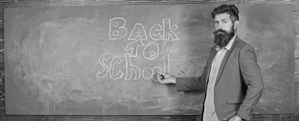 Teacher passionate job ability reach out students. Man bearded teacher missed his work during vacation. Back to school concept. Teacher near chalkboard holds chalk write inscription back to school