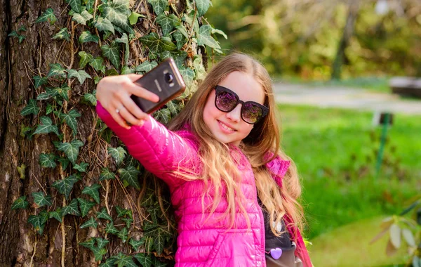 Bonita selfie. La niña pasa tiempo libre en el parque. niño feliz en el parque. Verano. Belleza natural. Felicidad infantil. hacer selfie en el teléfono. Medio ambiente verde. planta trepadora en el árbol con hojas de hiedra — Foto de Stock