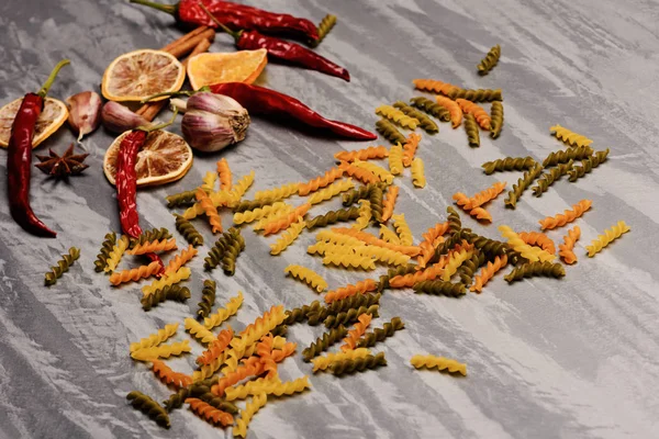 Delicious colorful Italian pasta with chili pepper, orange, garlic, star anise and cinnamon on grey textured background, side vie — Stock Photo, Image