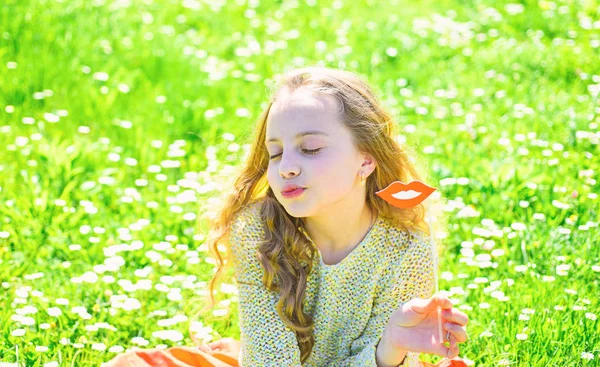 Conceito de beijo. Menina no rosto beijando passar o lazer ao ar livre. Criança posando com papelão boca sorridente. Menina senta-se na grama no grassplot, fundo verde — Fotografia de Stock