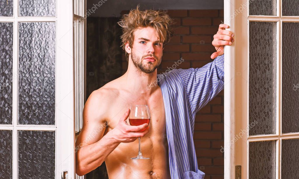 Man with sexy torso drink wine. Sexy lover concept. Bachelor sexy body chest and belly. Guy shimmering sweaty skin wear bathrobe. Sexy attractive macho tousled hair coming out through bedroom door