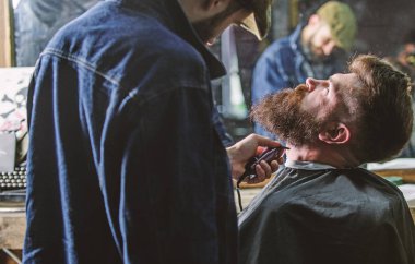 Sakal hipster istemcisinin, ayna yansıma arka plan üzerinde damat ile meşgul berber. Sakallı hippi cape kırpma şık berber dükkanı olarak profesyonel kuaför tarafından kaplı. Damat kavramı