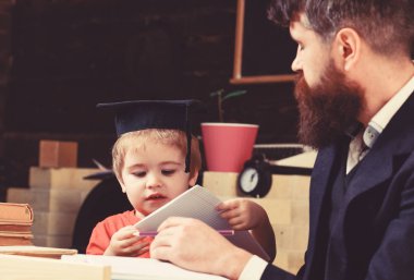 İlköğretim kavramı. Çocuk çalışmaları dikkatle dinlerken öğretmen ile. Öğretmen ve öğrenci kolej, kara tahta arka plan içinde. Baba oğul öğretir temel bilgi, tartışmak, açıklamak