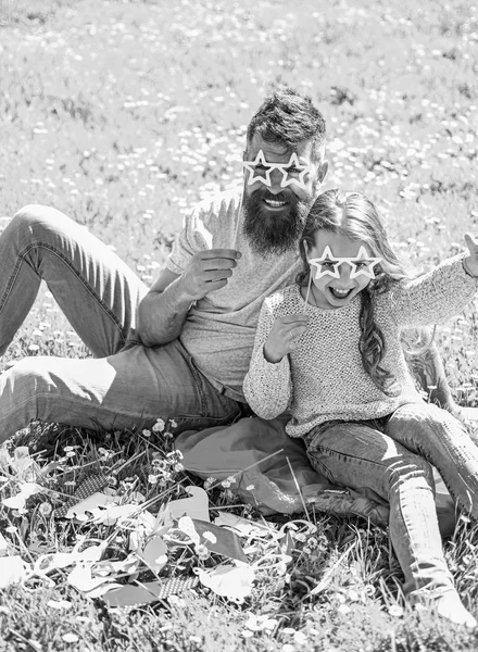 Père et fille sont assis sur l'herbe à la prairie, fond vert. Enfant et papa posant avec des lunettes en forme d'étoile attribut photomaton au pré. La famille passe ses loisirs à l'extérieur. Concept de superstar — Photo