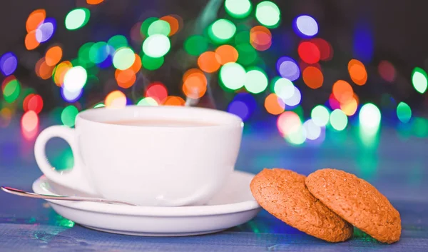 Fresh brewed coffee in white cup or mug on defocused garland lights background. Coffee drink winter holiday new year. Enjoying coffee on christmas morning. Coffee time christmas eve