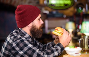 Bar rahatlamak ve içmek için rahatlatıcı bir yer. Sakallı adam bira içer hamburger menüsü yer. Barda afiyet olsun. Barda oturan vahşi hippi sakallı adam. Yüksek kalorili atıştırmalık. Hipster barda dinleniyor.