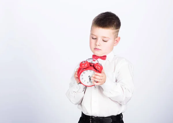 Nadszedł czas. Harmonogram i czas. Poranną rutynę. Uczeń z budzikiem. Kid urocza chłopiec biała koszula czerwona muszka. Rozwijać samodyscyplinę. Skonfiguruj budzik. Dziecko mały chłopiec trzymać czerwony zegar — Zdjęcie stockowe