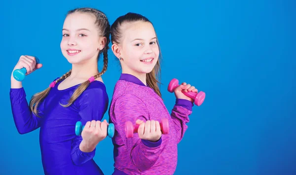 На пути к более сильному телу. Девушки тренируются с гантелями. Упражнения гантели для начинающих. Спортивное воспитание. Дети держат гантели на синем фоне. Спорт для подростков. Легкие упражнения с гантелями — стоковое фото