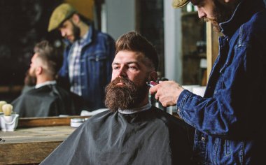 Sakallı hippi cape kırpma şık berber dükkanı olarak profesyonel kuaför tarafından kaplı. Damat kavramı. Sakal hipster istemcisinin, ayna yansıma arka plan üzerinde damat ile meşgul berber