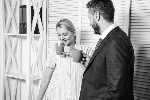 Dois de empresários atraentes, de pé ao lado um do outro, segurando uma xícara, sorrindo de pé no escritório. Entrevista de emprego. Duas pessoas casuais . — Fotografia de Stock