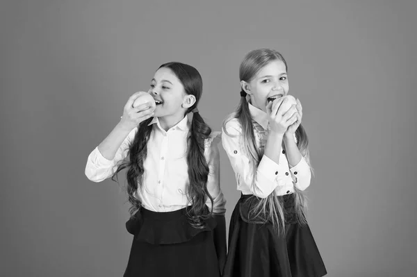 Schoolgirls eat apples. School lunch. Vitamin nutrition during school day. Boost student acceptance of fruit. Distributing free fresh fruit at school. Girls kids school uniform orange background — Stock Photo, Image