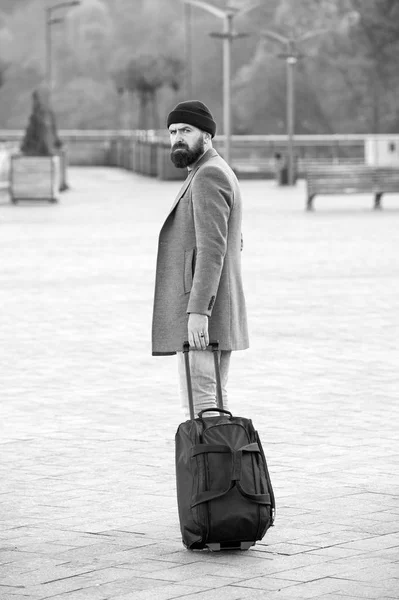 Hipster ready enjoy travel. Carry travel bag. Man bearded hipster travel with luggage bag on wheels. Adjust living in new city. Traveler with suitcase arrive airport railway station urban background