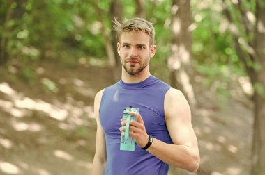 Sporcu erkek sporcu idmandan sonra şişeye su döker. Harika bir egzersizden sonra vitamin içeceğini tazeliyorum. Sporcu parktaki eğitimden sonra su içer. Adam atletik görünüşte su şişesi tutuyor.