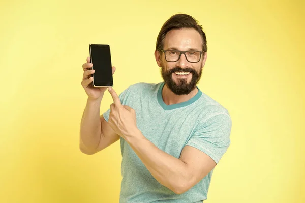 Man excited about new mobile opportunities. Guy eyeglasses cheerful pointing at smartphone. Man happy user interact application for smartphone. Guy bearded interact mobile interface application