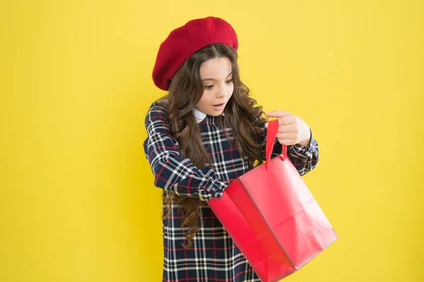 Sólo un minuto de sorpresa. Niña buscando un regalo sorpresa sobre fondo amarillo. Niño pequeño sosteniendo bolsa de compras con sorpresa. Adorable comprador con emoción sorpresa en la cara —  Fotos de Stock