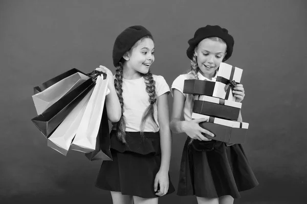 Concepto Shopaholic. Las compras se vuelven divertidas con los mejores amigos. Niños lindas colegialas sostienen manojo bolsas de compras. Niños satisfechos comprando fondo rojo. Obsesionado con centros comerciales y de ropa —  Fotos de Stock