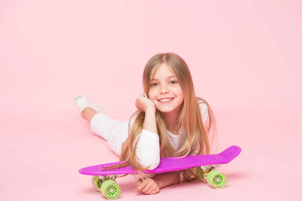 Niño adorable niño pelo largo adoro paseo penny board. Feliz infancia. Montar tablero de peniques y hacer trucos. A la chica le gusta andar en monopatín. Estilo de vida activo. Chica divirtiéndose con penny board fondo rosa — Foto de Stock