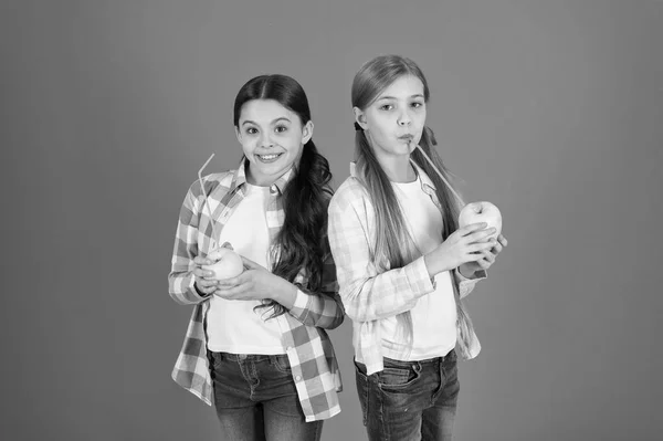 Las colegialas comen fruta de manzana. Almuerzo escolar. Nutrición de frutas con vitaminas para niños. Estilo de vida saludable. Distribuyendo fruta fresca gratis en la escuela. Chicas niños estilo casual comer fruta manzana fondo naranja —  Fotos de Stock