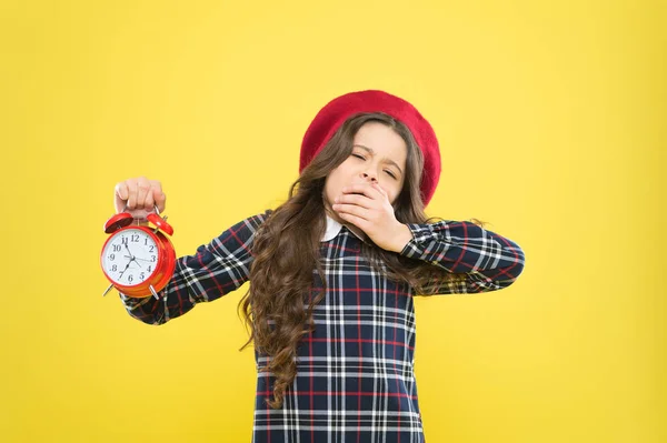 Het is tijd om te gaan slapen. Slaperig klein meisje in de avond tijd op gele achtergrond. Gaap klein kind met wekker. Te laat. Rusttijd, fris jezelf op. — Stockfoto