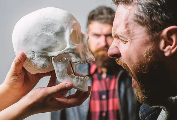 Psychology concept. Human fears and courage. Looking deep into eyes of your fear. Man brutal bearded hipster looking at skull symbol of death. Overcome your fears. Be brave. Focused on breaking fear