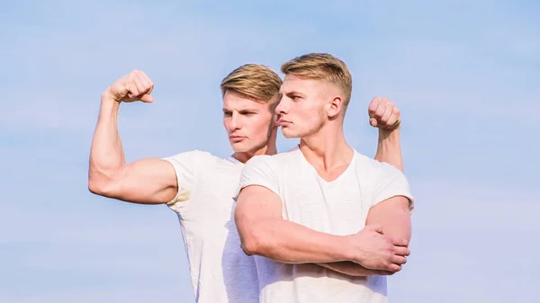 Des jumeaux séduisants. Beaux jumeaux forts. Hommes jumeaux frères musclés fond ciel. Homme musclé musclé bodybuilder athlète posant avec confiance dans des chemises blanches. Mode de vie sportif et corps sain — Photo