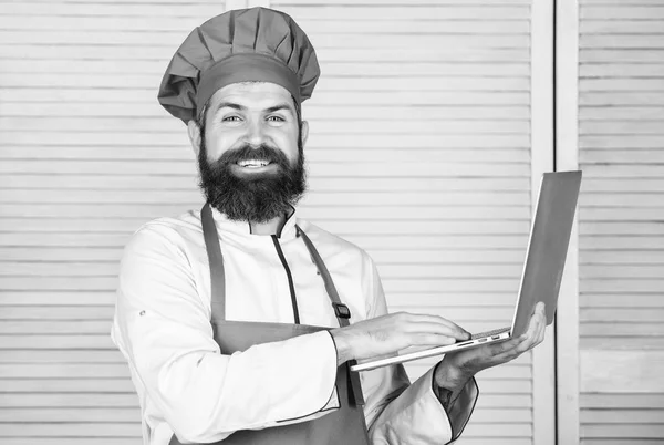 Kruidenier online. Verzendingsdienst. De laptop van de chef-kok in de keuken. Culinaire school. Hipster in hoed en schort producten online kopen. Online winkelen. Man chef-kok online ingrediënten koken voedsel zoeken — Stockfoto