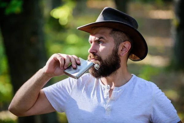 Hipster with beard drink alcohol nature background defocused. Hiking camping. Wanderer concept. Alcohol drink. Nomadic man carry alcohol with him. Guy brutal bearded cowboy drink alcohol metal flask — Stock Photo, Image