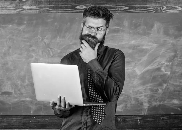 Distance education concept. Surfing internet. Hipster teacher wear eyeglasses and necktie holds laptop surfing internet. Teacher bearded man with modern laptop surfing internet chalkboard background — Stock Photo, Image