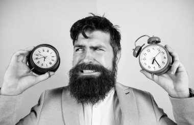 Does changing clock mess with your health. Man bearded hipster hold two different clocks. Guy unshaven puzzled face having problems with changing time. Time zone. Changing time zones affect health
