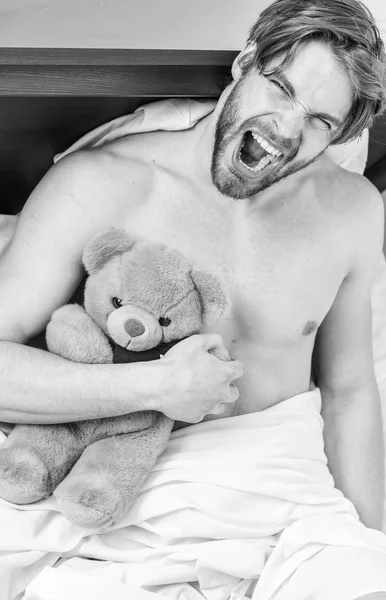 Guy hug teddy bear soft plush toy. Man unshaven bearded face relax with favorite teddy bear. Sweet memories from childhood. Sweet dreams concept. Man handsome guy relaxing bed hug teddy bear toy