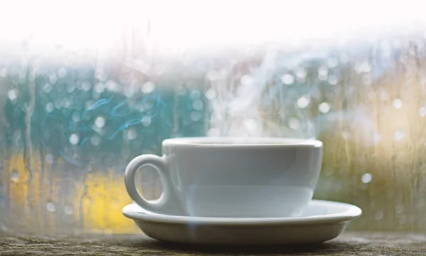 Fresh brewed coffee in white cup or mug on windowsill. Wet glass window and cup of hot coffee. Autumn cloudy weather better with caffeine drink. Enjoying coffee on rainy day. Coffee time on rainy day