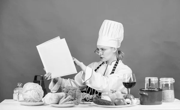 Mujer cocinera cocinando comida saludable. Chica leer libro mejores recetas culinarias. Concepto de escuela culinaria. Mujer en sombrero y delantal sabe todo sobre artes culinarias. Cocina tradicional. Experto culinario —  Fotos de Stock