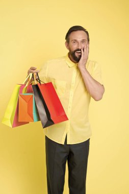 Olgun sakallı, neşeli yüzlü bir adam alışveriş torbaları tutuyor. Adamın beklenmedik yetenekleri var. Hediye sarısı arka plana şaşıran adam. Hediyeler hayatımızı daha ilginç kılıyor. Müşteri için ikramiye her zaman iyi fikirdir.