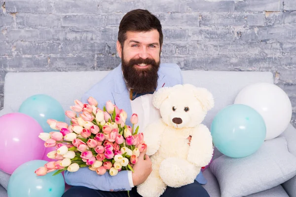 Romantic gift. Macho ready romantic date. Man wear blue tuxedo bow tie hold flowers bouquet. Romantic man with flowers and teddy bear sit on couch waiting girlfriend. How successfully ask her dating