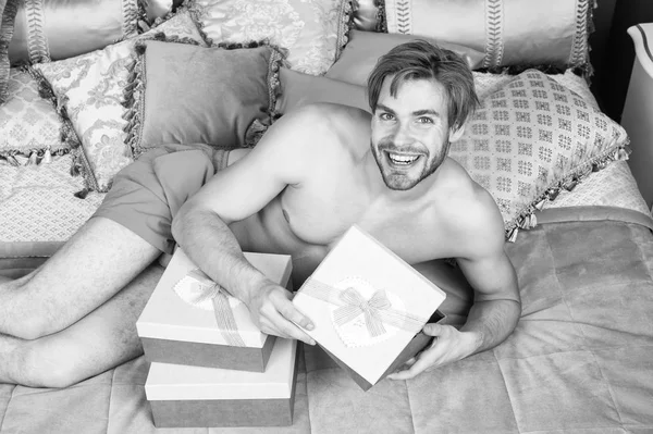 A abrir o seu presente. Bonitão com caixa na manhã de aniversário. Homem sexy sorrindo com presente de aniversário na cama. Homem feliz segurando presente de aniversário embrulhado em caixa. Feliz aniversário para você — Fotografia de Stock