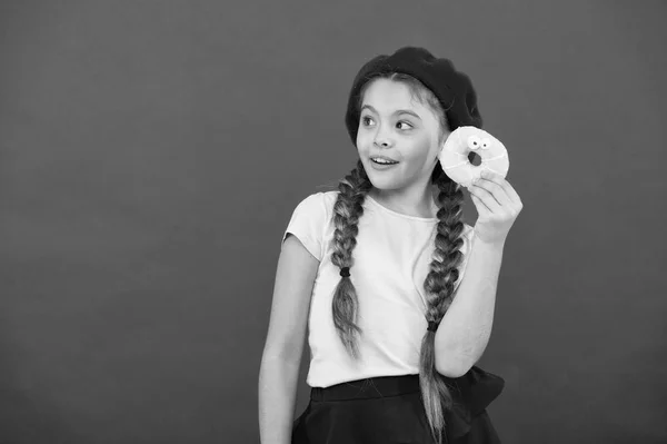 Kind speels meisje klaar om te eten van de donut. Snoepjes winkel en bakkerij concept. Kinderen enorme fans van gebakken donuts. Onmogelijk om te weerstaan vers gemaakt donut. Meisje houdt geglazuurde schattig donut in de hand rode achtergrond — Stockfoto