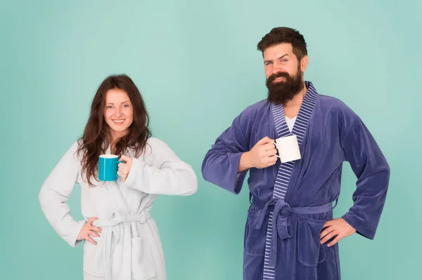 Chaque matin commence par un café. Couple en peignoirs avec des tasses. Homme barbu et femme endormie dégustent du café ou du thé le matin. Le type en tenue de bain tient du thé café. Commencez une nouvelle journée. Concept petit déjeuner — Photo