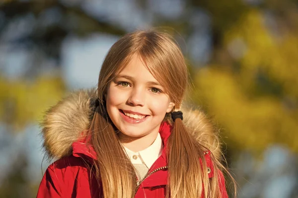 Niña disfrutar del día de otoño. Niño rubio pelo largo caminando en chaqueta caliente al aire libre. Chica encantadora chaqueta sonrisa disfrutar de parque de otoño. Los niños usan abrigo de moda con capucha. Ropa de otoño y concepto de moda —  Fotos de Stock