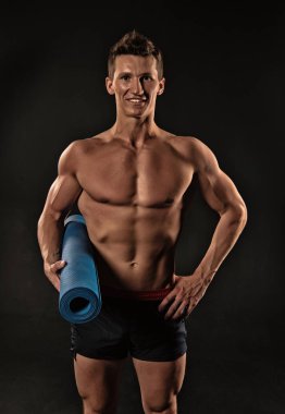 Mutlu bir adam yoga mat tutun. Sporcu gülümseme seksi gövde ve altı paketi ile. Atlet şort güçlü kollarıyla gülümseyerek. Spor salonu ekipman eğitim ve egzersiz için. Spor yoga ve fitness aktivitesi, vintage