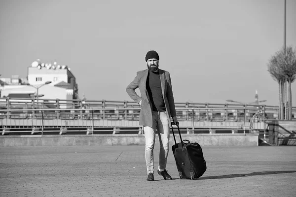 Moving to new city alone. Hipster ready enjoy travel. Carry travel bag. Man bearded hipster travel with luggage bag on wheels. Traveler with suitcase arrive airport railway station urban background