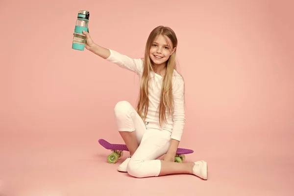 子供女の子ケア体水分補給します。アクティブなレジャーと水のバランス。アクティブで健康的な子供は、水を飲む。水和滞在します。女の子の幸せそうな顔を座っているペニー ボード ピンク背景中の水のボトルを保持します。 — ストック写真