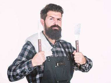 Barbekü ustası. Sakallı hippi barbekü için önlük giyer. Kızartma ve ızgara yemek. Adam mutfak aletlerini barbeküde tutuyor. Açık havada et kızartmak için aletler. Piknik ve barbekü. Parkta et pişiriyorum.